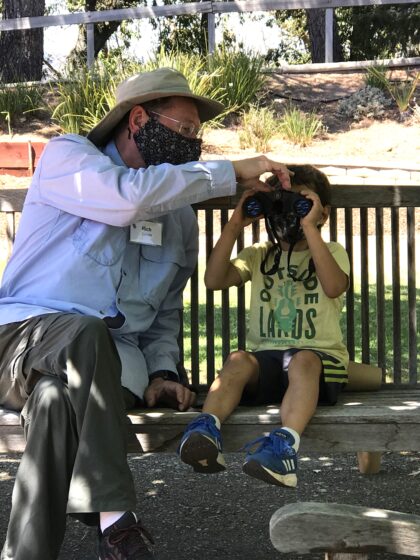 Adult male showing little boy how to use binoculars.