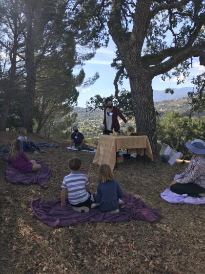 Picture of children in a circle for the Harvest celebration out under the oak tree.