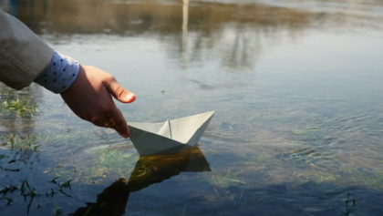 hand placing paper boat in the water