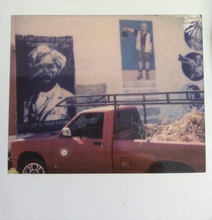 There is a farm pickup truck parked in front of a wall with posters of men.