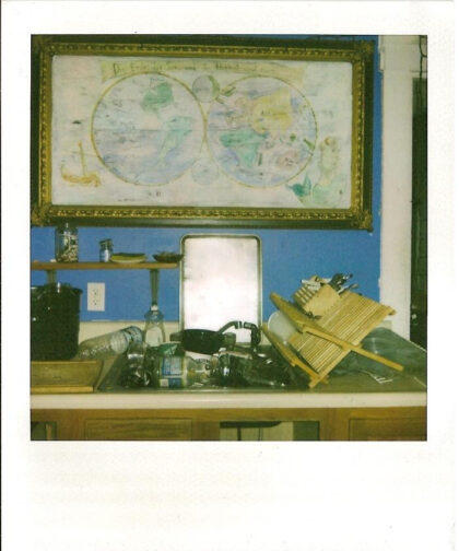 A sink full of dishes, a drying rack, and a world map on the wall.