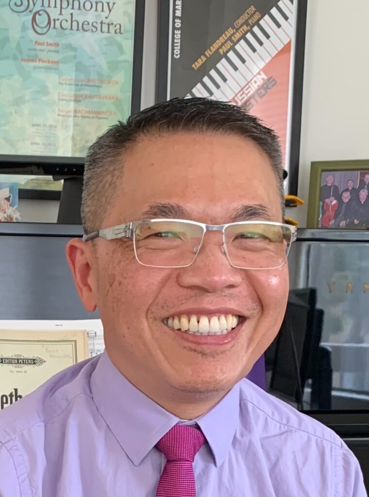 smiling head shot of Milton in his shirt and tie, wearing glasses