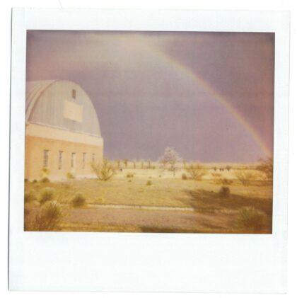 a rainbow arching over a Quonset style building with sparse vegetation.