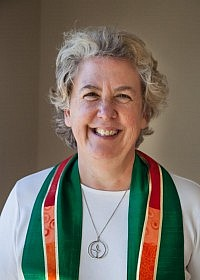 Rev Lucy Bunch wearing a white top with a UU necklace and a green and red stole.