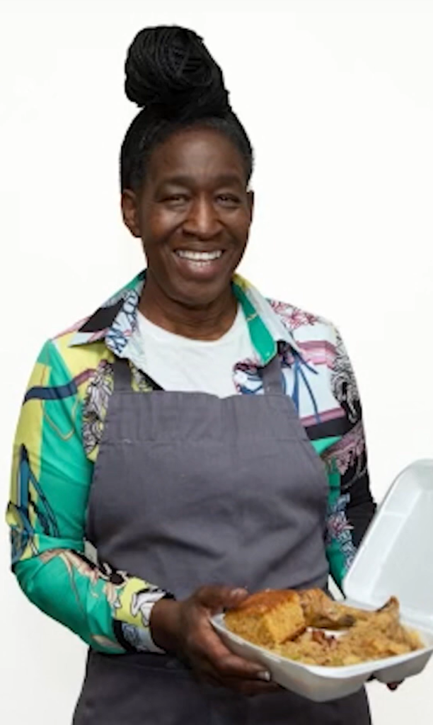 Sandra McMillion in an apron holding a box of soul food.