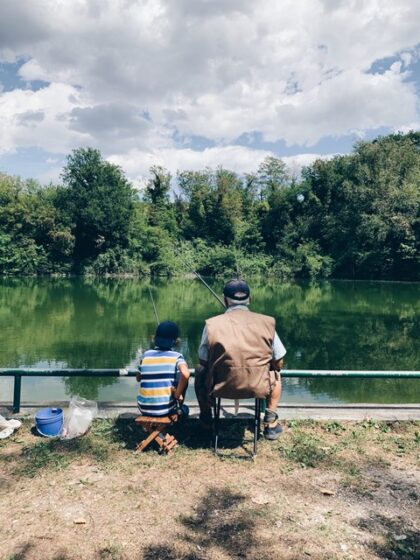 Adult and child fishing on a river bank.