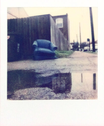 Old blue recliner discarded next to a dumpster in a rainy lot.