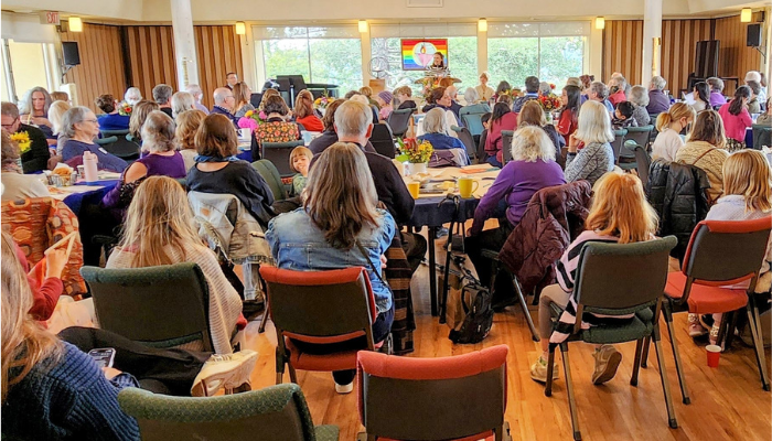 Large audience at many round tables listening to a speaker.