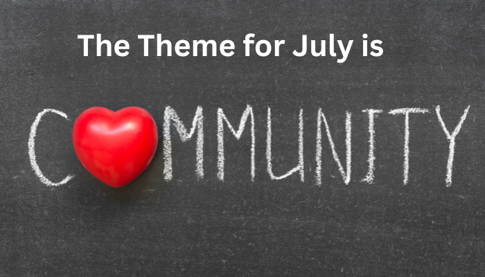 A blackboard with writing in chalk that says The theme for July is Community. The O is replaced by a red heart.