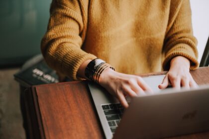 A woman in a yellow sweater is typing on a laptop.