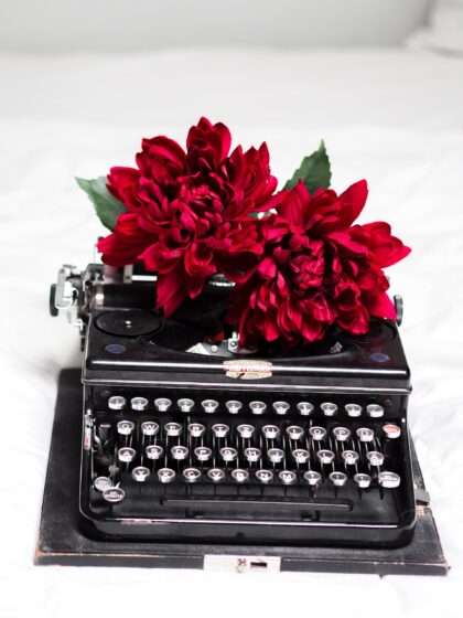 black typewriter wearing a crown of bright red flowers.